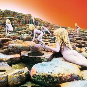 Six nude children with long blonde hair scramble up a stairstep series of basalt rocks ascending away from the viewer, with an orange-white sky above